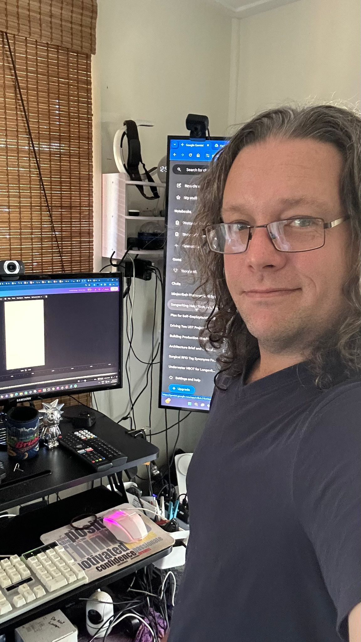 Luke Nathan Hayes with long hair and glasses at his office desk.