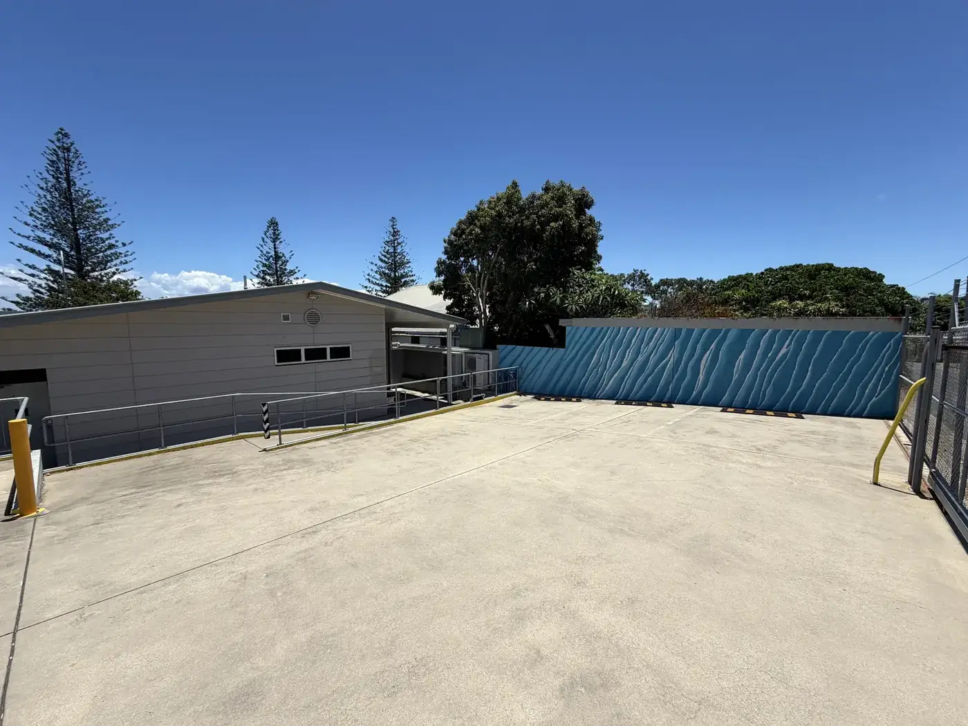 Supplied reference photo of the rear parking and loading area with concrete surface, blue wall and service access.