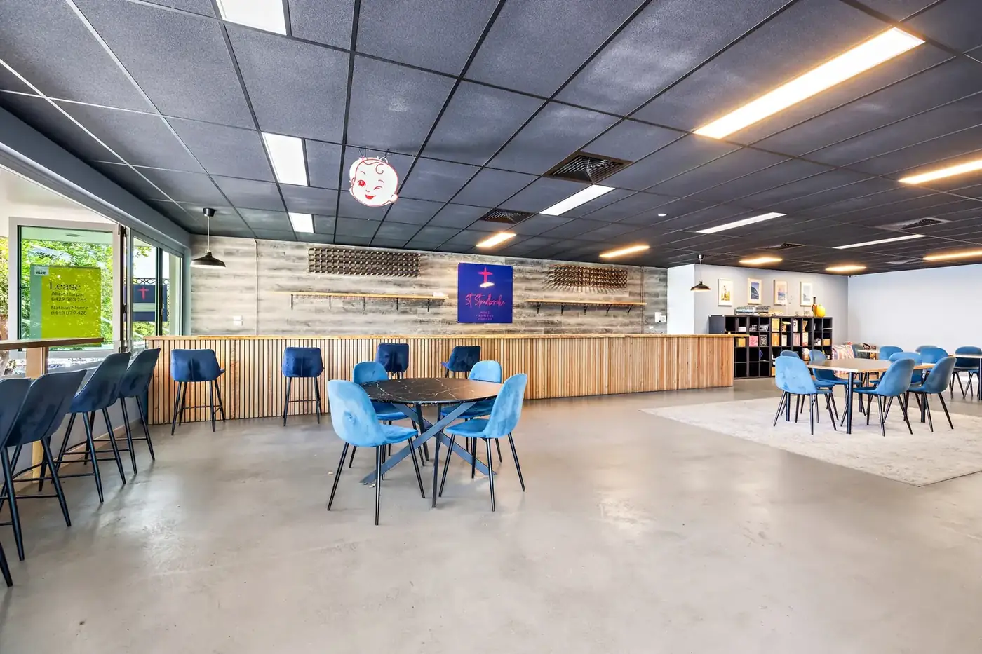 Supplied reference photo of the open main room with black ceiling grid, timber counter, blue chairs and large windows.