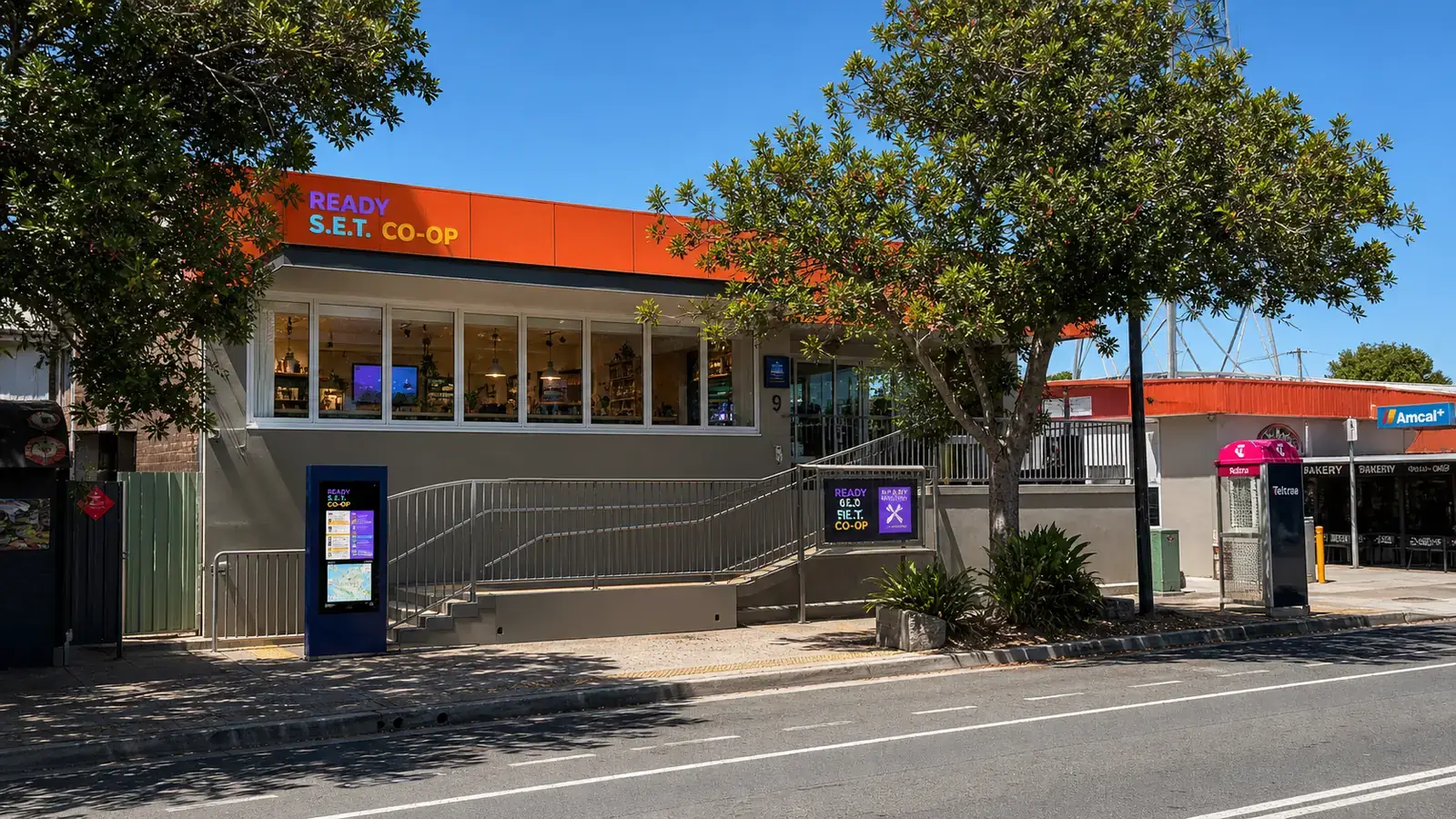 Generated concept image based on the 9 Ballow Road frontage, showing the orange fascia, street tree, entry ramp, co-op kiosk and community hub activity.