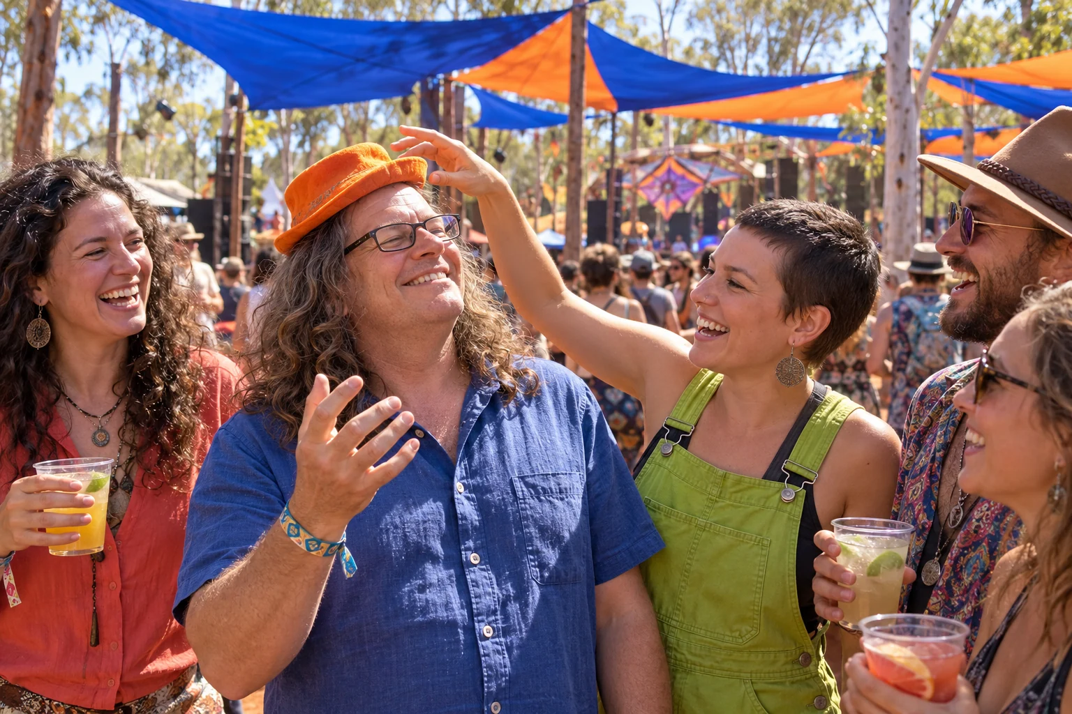 Long-haired Tiggy laughs with adult friends as a woman playfully tilts his orange hat at an imagined outdoor festival.