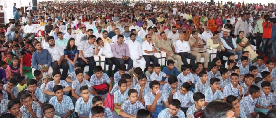 A large crowd of school students seated in a field watching the rocket demonstration