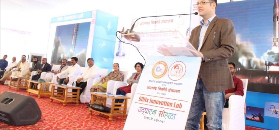 Luke Nathan Hayes speaking at a lectern on the SDNx Innovation Lab stage, with dignitaries seated behind him