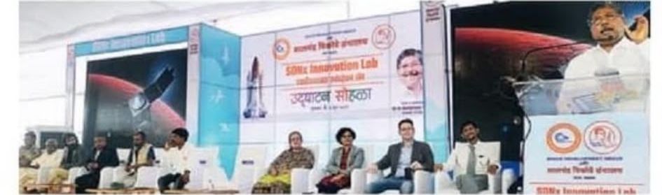 Wide view of the SDNx Innovation Lab stage with the panel seated and rocket imagery on the backdrop